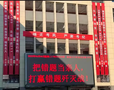 教学楼外悬挂多条红色励志横幅，左侧有“高分考入985”“从容应考笑傲群雄”等标语，右侧有“蟾宫折桂金榜题名”“为青春致贺向清华进军”等内容，中部横挂“端正考风 严肃考纪”横幅。楼下电子屏显示时间为2023年6月6日17时40分50秒，提示“距离2023年高考仅剩00天”，并醒目展示“把错题当亲人，打赢错题歼灭战！”的口号，整体呈现高考前夕学校浓厚的备考动员氛围。