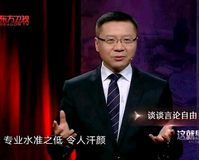 图片显示一名穿着西装、戴着眼镜的男性主持人正在东方卫视的节目中发言。他表情严肃，双手摊开，背景为深色幕布和紫色调舞台设计。屏幕上有“谈谈言论自由”的标题文字，底部配有“专业水准之低 令人汗颜”的字幕内容。左上角可见东方卫视的红色台标。