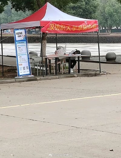 图片中是一个大学的临时帐篷，红色横幅上写有“汉纺组织大学早起协会”。帐篷下有两位成员坐在桌前，其中一人趴在桌上睡觉，另一人也低头休息，看起来非常困倦，形成了“早起协会成员却在睡觉”的强烈反差，非常搞笑，讽刺了早起协会名不副实。此场景充满校园生活气息，也明显有自嘲和幽默的成分。此图常被用来自嘲组织或者活动做表面功夫、参与者积极性低，实际情况与宣传目的相反。

有较为明显的双关和反讽：表面上是“早起协会”，实际成员却困得不行，早起协会不起反而睡觉，体现了现实与理想的反差，有一定的讽刺意味。