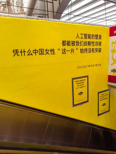 这是拍摄于地铁扶梯旁的自由点卫生巾品牌广告，以醒目的黄色为背景，通过对比中国在人工智能、高铁、青蒿素等高端科技领域的突破，发出「凭什么中国女性“这一片”始终没有突破」的质问，传递品牌要突破女性护理用品技术壁垒的决心。广告同时做出「“0”病菌，“0”致敏」的产品承诺，下方两个小框补充文案分别以中国高铁世界第一、青蒿素获诺贝尔奖的案例，进一步强化中国有能力打造高端女性护理产品的观点，整体文案采用对比式的表达，引发受众对女性护理品技术标准的关注，突出品牌的技术升级理念。