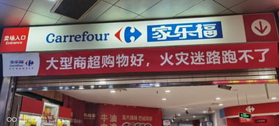 这是一张家乐福超市卖场入口的实拍图，入口上方是带有蓝白红配色的家乐福（Carrefour）品牌标识，左侧标注“卖场入口 Entrance”。入口处悬挂一条醒目的红色横幅，上面写着“大型商超购物好，火灾迷路跑不了”，此处运用了谐音梗，“跑不了”谐音双关，字面意思是火灾迷路就无法逃生，和前半句的“购物好”形成反差，略带调侃意味，让严肃的消防安全提醒变得诙谐。入口内部可见超市的部分区域，还有其他宣传横幅，如写有“牛油”“五大风味 巴适得很”的川味风格横幅，显示出超市的商品特色。左下角带有HUAWEI P40 Pro 5G的拍摄标识，表明图片由该手机拍摄。