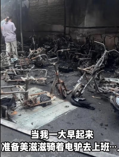 图中是一片电动车停放场，几乎所有电动车都被严重烧毁，仅剩下焦黑的车架。前景处有明显的烧焦痕迹，背景中有两位疑似失主在观察现场。图片底部配有幽默感的文字：“当我一大早起来准备美滋滋骑着电驴去上班…”，形成明显的反差和无奈的氛围，戳中打工人的心态，有一定的黑色幽默。

涉及“美滋滋”与“电驴烧毁”的极强对比，属于生活中突发的无语但又带点自嘲的场面。无明显谐音梗，但讽刺意味明显。