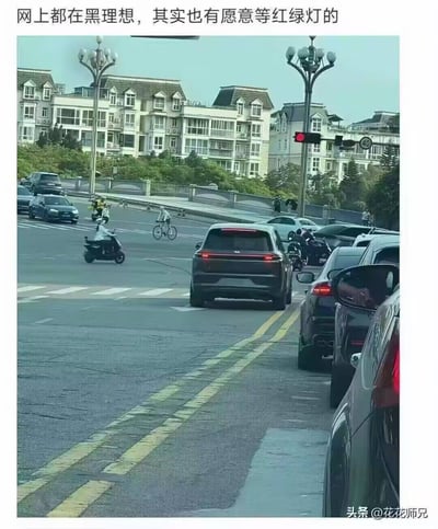 这是一张顶部配文的实拍梗图，顶部文字为“网上都在黑理想，其实也有愿意等红绿灯的”，下方画面为城市十字路口红灯亮起的场景，一辆理想品牌的深色SUV正停在停止线前等待通行，路口还有其他行驶的机动车、电动车、自行车，路旁是多栋欧式外观的居民住宅楼，道路两侧设有造型复古的路灯，图片右下角带有“头条@花花师兄”的水印。该图用反讽的语气调侃此前网络上流传的理想汽车辅助驾驶系统无法正确识别红绿灯、易出现闯红灯违规行为的负面舆情。