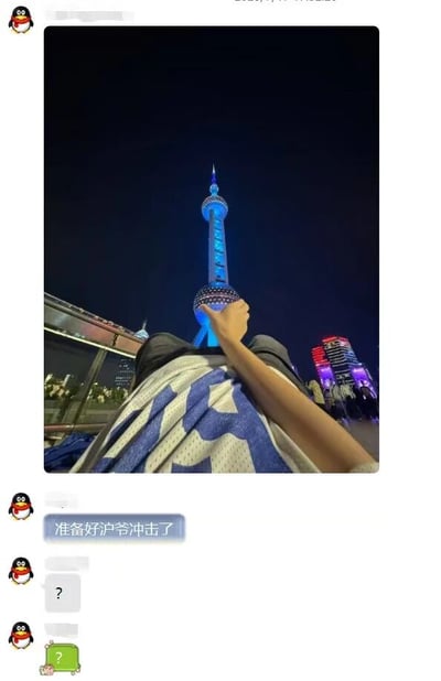 这张图片展示了上海东方明珠塔的夜景，塔身被蓝色灯光照亮，在夜空中格外醒目。图片采用第一人称视角，拍摄者正坐在地上，一只手伸出指向东方明珠塔，身上盖着蓝白相间的球衣。图片下方是QQ聊天界面截图，包含一条消息“准备好沪爷冲击了”以及后续的问号回应。
