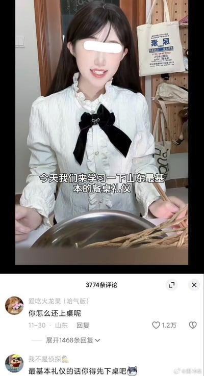 图片为竖屏手机格式的社交媒体视频截图，画面中一位穿着白色带黑色蝴蝶结衬衫的女性坐在桌前，面前放着一个金属大碗和一些长条状物品（疑似食材或餐具）。图中叠加文字写着“今天我们来学习一下山东最基本的餐桌礼仪”，营造出一本正经教学的氛围。下方评论区有用户调侃“你怎么还上桌呢”“最基本礼仪的话你得先下桌吧”，通过反差形成强烈的反讽幽默效果，吐槽所谓的“餐桌礼仪”可能存在的刻板印象或荒谬之处。