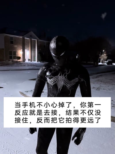 这是一张顶配底文的搞笑梗图，画面背景是夜晚积雪的居民区，主体是一位真人Cosplay的毒液共生体蜘蛛侠，他身着黑色带白色纹路的战衣，站在雪地中，姿态看起来懊恼又无奈。图片下方的配文描述了一个很多人都经历过的日常尴尬场景：手机掉落时下意识去接，却失误把手机拍得更远，用这个经典的超级英雄懊恼形象来放大这种小失误带来的无奈感，引发观者的共鸣。