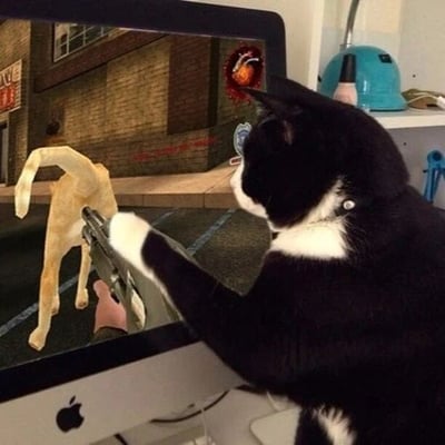 一只黑白相间的猫咪正坐在苹果iMac电脑前，全神贯注地盯着屏幕。屏幕显示第一人称射击游戏画面：砖墙街道背景中，左侧有黄色狗角色，右上角有红色爆炸特效。猫咪前爪恰好放在屏幕虚拟手枪位置，仿佛紧握枪支瞄准目标。电脑旁架子上有蓝色安全帽等物品，通过猫咪姿势与游戏画面的巧妙结合，营造出“猫咪玩游戏”的幽默拟人效果。