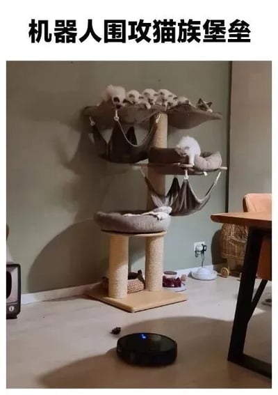 图片展示了一个多层猫树，上面趴着多只猫咪，如同猫族的堡垒。猫树下方的地板上，一台黑色的机器人吸尘器正在工作，仿佛一个围攻堡垒的机器人。图片上方配有文字“机器人围攻猫族堡垒”，通过拟人化的幽默手法，将日常场景转化为有趣的“攻防戏码”，猫咪们悠闲的姿态与机器人吸尘器的“进攻”形成鲜明对比，充满生活趣味。