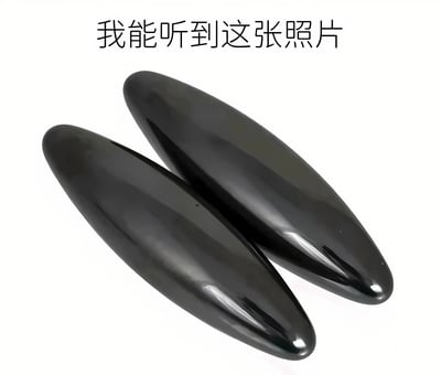 图片中央展示了两个黑色、表面光滑的椭圆状物体，放置在纯白色背景上。上方配有文字“我能听到这张照片”，形成一种视觉与听觉联想的幽默效果。这种表述是网络上常见的迷因格式，通过图像引发观者对特定声音的想象，通常用于调侃那些具有强烈声音联想的物品或场景。