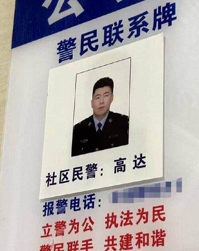 这是一张实拍的警民联系牌图片，牌面上方有蓝色的“警民联系牌”字样，中间位置是一位身着警服的男性民警的证件照，照片下方标注着“社区民警：高达”，其下方的报警电话被做了打码处理，牌面最底部是两行红色的宣传标语：“立警为公 执法为民”“警民联手 共建和谐”。由于民警的名字“高达”和知名日本动漫《机动战士高达》中的核心IP名称完全相同，形成了有趣的巧合，让原本严肃的警民联系牌带有了趣味性，容易引发网友的玩梗联想。