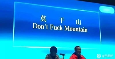 这是一张会议现场的屏幕截图，屏幕上显示中文地名“莫干山”，下方的英文翻译被恶意恶搞，利用“莫干”的谐音，将其翻译成了包含粗俗含义的“Don't Fuck Mountain”——“莫”对应“Don't”，“干”被低俗谐音成了不雅词汇，制造出荒诞搞笑又低俗的效果。屏幕下方有两位真人，处于会议场景中，看起来像是参会或发言人员，其中一位低头，面部被遮挡，另一位看向一侧，两人都坐在麦克风前，右下角带有“@吊图吧”的水印。