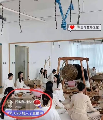 这是一张音疗直播的截图，画面中一群身着白衣的人围坐在摆放着颂钵、铜锣等音疗器具的房间内，正在进行音疗活动，氛围安静平和。画面下方的直播互动弹窗里，出现了带有男性头像的“我叫陈桂林 送鲜花”内容，和静谧的音疗场景形成强烈反差，增添了搞笑感。