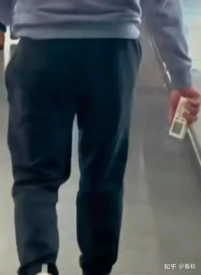 这张图片拍摄自一个人背影走路的瞬间，主角手中握着一个空调遥控器。图片通过幕后抓拍的形式，捕捉了一种日常但略显幽默的场景：很多人在家中懒得反复起身调空调，因此手拿遥控器满屋走。据网络语境，这种动作也被网友戏称为“全屋通杀”或“掌控全局”。这一行为画面，容易引发网友共鸣和调侃，具有生活化的幽默。没有明显的双关或谐音梗，但日常题材本身带有自嘲和实用性玩笑味道。