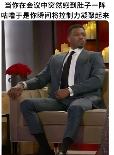 图片展示了一位穿着灰色西装的黑人男子正襟危坐的场景，背景有红色花朵和蜡烛营造出正式氛围。图片上方配有文字：'当你在会议中突然感到肚子一阵咕噜于是你瞬间将控制力凝聚起来'，通过男子严肃专注的表情与文字描述的尴尬生理状况形成幽默对比，展现了职场中常见的社死瞬间应对状态。