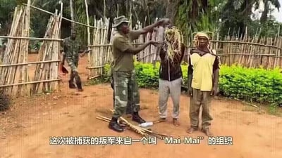 这是在非洲乡村土路上的抓捕现场，一名身着军装的武装人员正在摆弄一名被捆绑男子头上的植物类物品，旁边还站着另一名男子，后方还有一名武装人员手持物品走来。地面散落着竹制器具，背景是竹制围栏与绿植。图中字幕显示这两名男子是来自“Mai-Mai”组织的被捕叛军，场景氛围严肃，呈现出抓捕后的真实现场画面。
无双关、谐音梗或暗示内容。