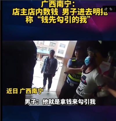 这张图是社会新闻的视频截图，顶部用黄色醒目字体标注事件概要：广西南宁一店主正在店内数钱时，有男子进入店内直接实施抢劫，被控制后该男子给出奇葩辩解，称“钱先勾引的我”。画面右侧可见涉事抢劫男子戴蓝色口罩，被身着警服的民警控制住，画面左侧门口有一名男子正看向店内方向，画面下方配有白色字幕，再次标注事发地为近日广西南宁，以及涉事男子的辩解内容。