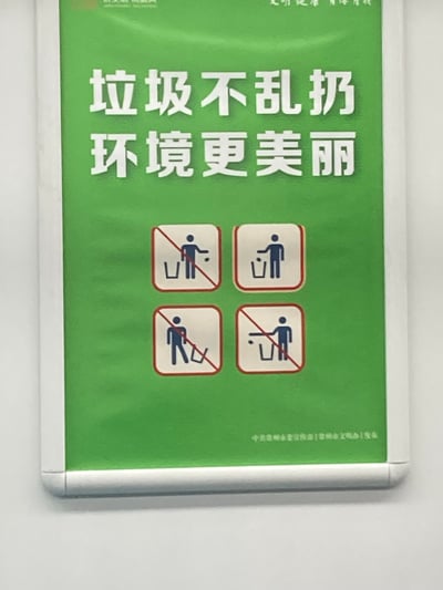这是一张竖版带边框的文明环保宣传海报，以绿色为背景，上方用醒目的白色大字标注核心标语“垃圾不乱扔 环境更美丽”。下方设置四个方形标识图标，直观展示了三种禁止行为（将垃圾扔到垃圾桶外、随手丢弃垃圾、垃圾扔在垃圾桶外）和一种正确行为（将垃圾投入垃圾桶），清晰传达规范投放垃圾的要求。海报底部标注了发布单位，整体设计简洁清晰，旨在倡导市民养成文明的垃圾投放习惯，共同维护整洁优美的环境。