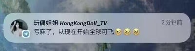 这是一张社交聊天记录截图，背景为模糊的风景图，界面中显示用户「玩偶姐姐HongKongDoll_TV」在2分钟前发布的消息：「亏麻了，从现在开始全球可飞😢😢😢」。
其中「亏麻了」是网络热词，指亏损程度非常严重；「全球可飞」结合发布者的成人向创作者身份，暗示其将开启全球范围的工作行程来弥补亏损，整体传递出发布者因亏损而无奈、沮丧的情绪。