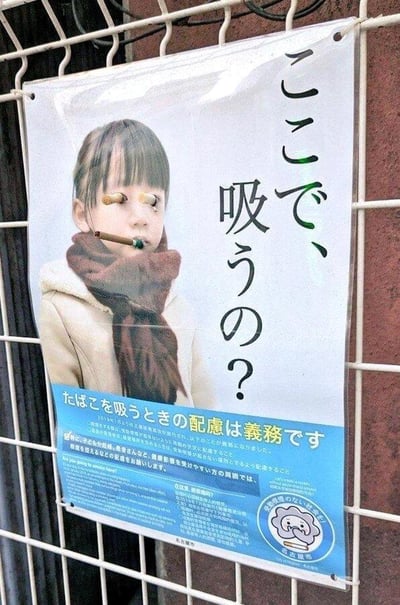 这是一张被网友二次创作恶搞的日本禁烟公益宣传海报，原本用于呼吁民众遵守吸烟礼仪、不在禁烟区域吸烟、保护他人健康的严肃海报，被添加了恶搞元素：海报里的小女孩眼部被贴上类似烟蒂的装饰，嘴里被P上了一支雪茄，配合海报上方的日文问句“在这里抽烟吗？”，形成强烈的反差搞笑效果。海报下方的蓝色区域保留了原本的禁烟宣传文字，写着“吸烟时的关怀是义务”，还有详细的吸烟注意事项说明，右下角还有带有卡通图案的“全面禁烟”标识，整体将原本严肃的公益宣传变成了充满戏谑感的恶搞图。
