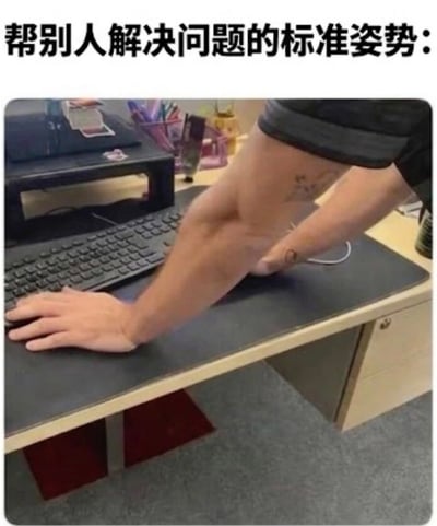 这是一张图文混排的职场趣味梗图，顶部配有文字“帮别人解决问题的标准姿势:”，下方的实拍图展现了办公室场景，一名手臂带有纹身的人半俯身探向工位桌面，一只手按在工位的键盘上，另一只手撑在桌面，呈现出帮同事操作电脑解决问题的姿势，桌面还可见键盘、笔筒等常见办公用品，该姿势精准还原了职场中同事间帮忙处理电脑问题时的常见状态，很容易引发职场人群的共鸣。