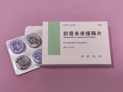 这张图片拍摄背景为粉色平面，主体是一款初音未来主题的恶搞文创周边：整体模仿口服缓释片的药品包装设计，白色药盒上印有产品相关文字信息，顶部明确标注“仅供娱乐 请勿食用”避免误食风险，盒身右下角印有四个绿色小爱心。从盒中取出的泡罩包装内的“药片”实际是圆形徽章，露出的4枚徽章上分别印有不同造型、不同服饰的Q版初音未来形象，创意感十足。