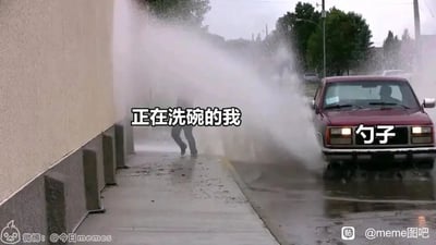 这是一张视频截图类的搞笑梗图，画面呈现的是路边水管破裂，大量水流喷涌而出，一名行人在水流中狼狈躲避的场景。图中通过文字标注，将这名行人标注为“正在洗碗的我”，将旁边的红色汽车标注为“勺子”，用这个夸张的现实场景，幽默地比喻人们在洗碗时，使用勺子清理碗中残渣时会溅出大量的水，自己就像图中的行人一样被水溅得狼狈不堪，用夸张的反差感来放大日常生活中的小尴尬，引发有类似经历的人的共鸣，制造出搞笑的效果。