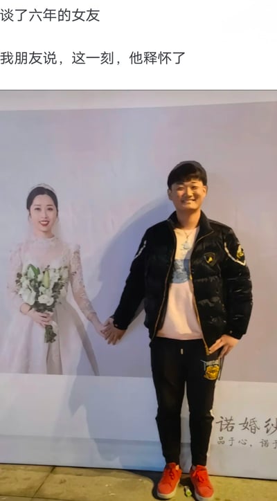 图中男子站在印有婚纱照的背景板前，通过巧妙的站位制造出视觉错位效果，看起来仿佛正和背景板里穿着婚纱、手持花束的女子手牵手。配文标注该女子是男子谈了六年的前女友，男子面带开心的笑容，配文称“这一刻，他释怀了”。这张照片利用视觉错位营造出创意合影的效果，传递出对过去感情放下的释然感。