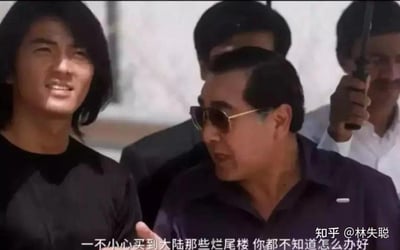 这是一张基于香港经典黑帮电影《古惑仔》截图二次创作的梗图。画面左侧是饰演陈浩南的郑伊健，他面带笑容，侧身与身旁的社团长辈角色交谈；右侧的长辈角色戴着墨镜，侧头看向陈浩南，神态严肃。图中底部添加了吐槽房产问题的字幕：“一不小心买到大陆那些烂尾楼 你都不知道怎么办好”，用经典港片的对话场景来调侃现实中购买烂尾楼后的无奈与糟心，通过影视IP的熟悉感放大吐槽的共鸣感。