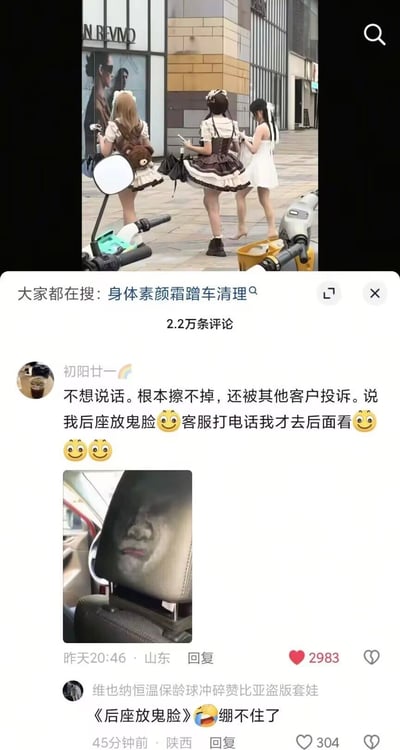 这张图是上下拼接的社交媒体内容截图，上方是街拍画面，展示了三位身着洛丽塔风格服饰的年轻女性背向镜头站在商业街区的路边，似乎在等候交通工具；下方是相关内容的评论区，显示共有2.2万条评论，热门评论由网约车司机用户“初阳廿一”发布，他吐槽自己搭载过穿这类服饰的乘客后，后座被乘客蹭上的粉底、素颜霜等彩妆痕迹根本无法清理干净，还被后续乘车的客户投诉，误以为他在后座放了鬼脸，自己直到接到客服的通知电话才去查看后座情况，同时附上了后座的实拍图，图中座椅上的彩妆痕迹恰好构成了一张类似人脸鬼脸的图案，语气十分无奈。第二条是其他网友的评论，调侃“后座放鬼脸”的说法，觉得这件事十分好笑。
