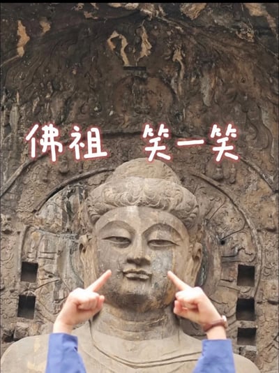 这张梗图取景于著名的佛教石刻造像，画面中“佛祖”上方加有手写体字：“佛祖 笑一笑”。下方有双手做出拉嘴角让佛祖“微笑”的动作，整体给人一种轻松幽默的气氛，带有对严肃文化景观的玩笑式解构和网络化表达。文案“佛祖笑一笑”有点调侃意味，常用于调节气氛、让严肃场合变得轻松。存在明显的情绪反转、神圣与搞笑的对撞。没有明显谐音梗，但有轻微的反差与双关调侃意味。