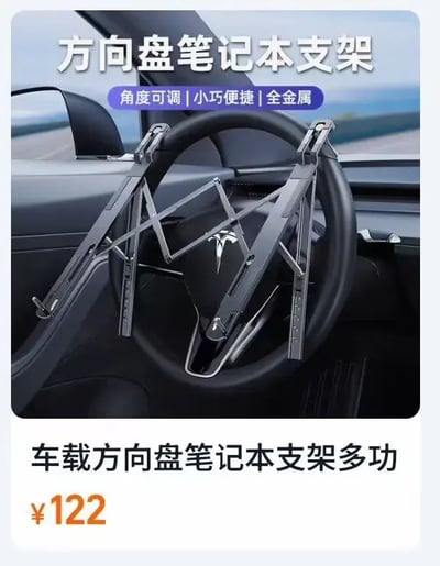 这是一张车载方向盘笔记本支架的促销图片，展示了支架安装在汽车方向盘（疑似特斯拉车型）上的场景。图片上方有大字标题“方向盘笔记本支架”，下方配有“角度可调 | 小巧便捷 | 全金属”的产品特点说明。图片底部标注了“车载方向盘笔记本支架多功”及价格“¥122”。整体画面以车内方向盘为主体，突出支架的安装方式和金属材质。