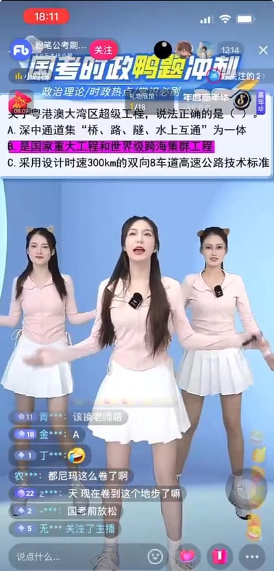 这是一张抖音平台粉笔公考刷题账号的直播画面截图，画面上方是国考时政押题的考题，内容为关于粤港澳大湾区超级工程的选择题；画面中间是三位穿着粉色上衣、白色短裙的女生在跳舞，试图用轻松的形式吸引考生；下方是直播间观众的弹幕，观众们纷纷吐槽现在公考备考太卷，还有观众给出答案选项。这是公考培训机构在国考冲刺阶段，采用娱乐+学习的创新直播形式，传递时政考点。