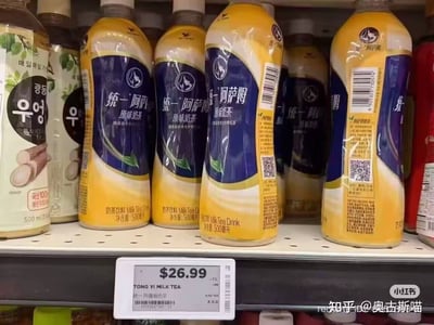 图片展示了超市货架的局部场景，中央位置整齐摆放着多瓶统一阿萨姆原味奶茶，每瓶净含量为500毫升。货架下方的价格标签显示该奶茶售价为26.99元。左侧货架上有其他品牌的饮料，瓶身上带有韩文标识；右侧也有部分饮料瓶身露出。图片右下角有“小红书”和“知乎@奥击斯喵”的水印标识。