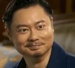 图片中是一位男性的肖像照，他留着深色短发，身着深蓝色外套，背景为室内环境，隐约可见沙发等家具，整体氛围显得比较日常自然。