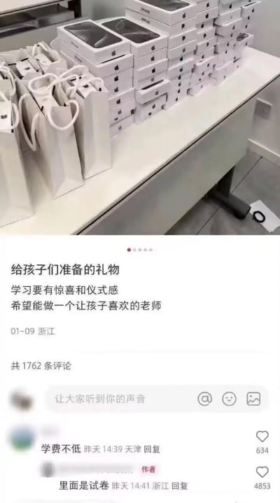 这是一张来自国内短视频社交平台的截图，上方实拍图展示了大量摆放在桌上的苹果产品包装盒及配套手提袋，配文称这是给孩子们准备的礼物，强调学习要有惊喜和仪式感，希望成为孩子喜欢的老师。评论区中，有网友调侃“学费不低”，作者回复“里面是试卷”，制造出强烈的反差感，用看似昂贵的电子产品包装装试卷，把“惊喜”变成了学生们的“惊吓”，充满搞笑效果。