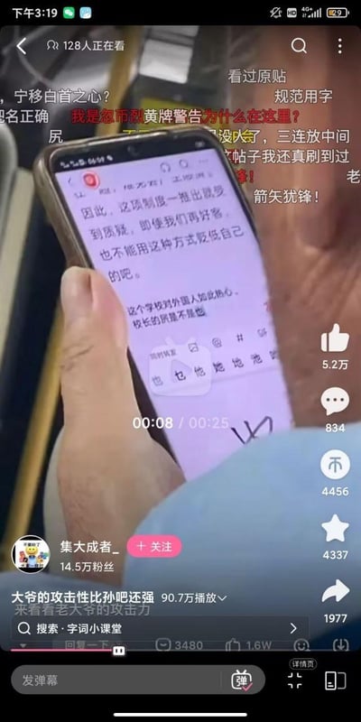 这是抖音平台的一段视频截图，画面中一位大爷用脚操作智能手机打字，手机屏幕上显示着一段犀利的评论，内容是质疑某学校针对外国人的相关制度，认为即便好客也不该贬低自身，还直言学校对外国人过于热心，措辞尖锐。视频配文称“大爷的攻击性比孙吧还强”，页面带有大量观众弹幕，右侧是抖音的点赞、评论、分享等互动按钮，视频作者为抖音用户“集大成者_”，该视频已有90.7万播放量，引发不少关注。
