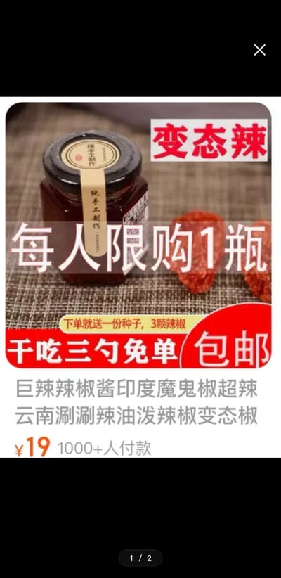 这是一张竖屏的电商平台商品宣传静态图，图中主体是一瓶标注“纯手工制作”的深褐色辣椒酱，旁边摆放着两颗印度魔鬼椒（云南涮涮辣）实物。图中用醒目的红色字体标注“变态辣”以突出产品的超辣属性，白色大字覆盖画面标注“每人限购1瓶”营造稀缺感，下方红色区域标注“干吃三勺免单 包邮”以及“下单就送一份种子，3颗辣椒”的购买福利，底部文字说明该辣椒酱是采用印度魔鬼椒、云南涮涮辣制作的超辣油泼辣椒产品，售价19元，已有1000+人付款。整体画面通过突出超辣属性、限购规则、免单福利等卖点，吸引喜爱超辣食品的消费者购买。