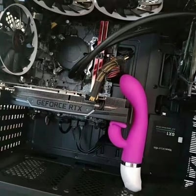 一张电脑主机内部的照片，展示了一个安装了GeForce RTX显卡的机箱内部。画面中央偏右位置，有一个粉红色的、形状类似性玩具的物体被插入显卡插槽中，与周围的黑色电脑硬件形成鲜明对比。机箱顶部可以看到多个散热风扇，右下角有TeamGroup的标识。这张图片通过将情趣用品与高端电脑硬件并置，创造出一种荒诞、搞笑的视觉效果。