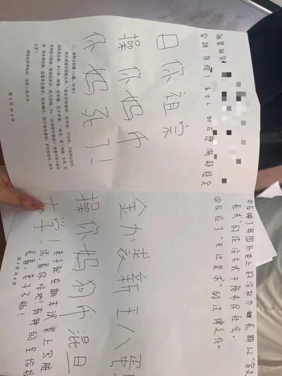 Image shows a hand holding paper with offensive handwritten Chinese text targeting someone's mother, including phrases like '操你妈' (fuck your mother) and '你妈死了' (your mother is dead). The paper appears to be part of a school assignment or exam with some printed text partially visible and some sections blurred with black squares.