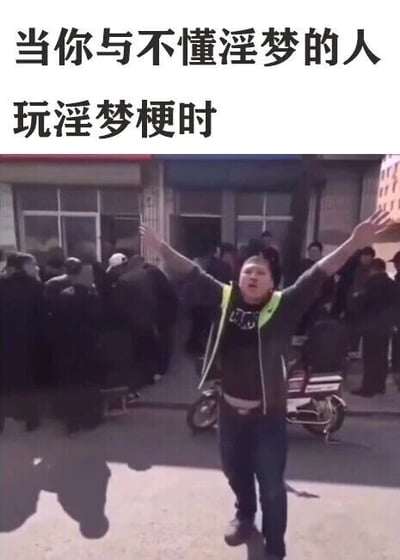这是一张图文混排的二次创作梗图，图片上方配有白色文字“当你与不懂淫梦的人玩淫梦梗时”，下方是一段街头场景的视频截图：画面中央是一名穿着带荧光绿反光条的深色外套、内搭深色上衣的男子，他双臂高高举起，表情激动，似乎在卖力地表达什么；男子身后是聚集的人群和一辆电动车，背景是临街的普通建筑。这张图用男子这种自我投入却无人呼应的状态，生动比喻了当淫梦梗爱好者向不了解该亚文化的人玩相关梗时，自己热情满满但对方无法理解、毫无共鸣的尴尬处境，精准戳中了亚文化圈子里玩梗遇冷的情绪。