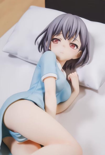 图中是一款二次元风格的美少女手办，角色有着灰紫色短发与泛红的委屈眼眸，身着浅蓝色短袖睡衣，侧趴在铺有白色床品的床上，一只手轻靠在枕头上，神态低落脆弱。手办细节刻画细腻，衣物褶皱、皮肤质感都表现出色，完美还原了少女低落委屈的状态。