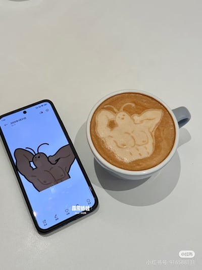 图片展示了一杯咖啡和一部手机的组合。手机屏幕上显示着一个肌肉发达的蟑螂卡通形象，有着明显的双马尾触角；旁边的咖啡上则有一个可爱风格的蟑螂拉花，同样突出了标志性的双马尾触角。这种将"广式双马尾"梗融入日常场景的创意，展现了网友对该 meme 的趣味演绎。