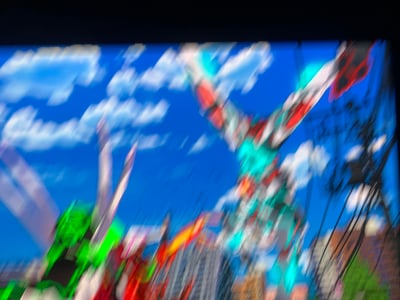 这是一张奥特曼系列动画的屏幕截图，画面带有强烈的动态模糊效果，呈现出奥特曼在城市上空的激烈战斗场景。画面右侧的白红青配色奥特曼处于高速行动状态，下方是城市建筑群，背景是蓝天白云，整体画面充满动感，营造出紧张刺激的战斗氛围。
