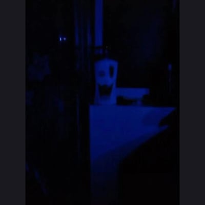 在昏暗的蓝色灯光环境里，一个放置在台面上的瓶子（看起来像是洗手液瓶），其瓶身的标签在光线和角度的影响下，形成了类似诡异笑脸的视觉效果，营造出有点惊悚又滑稽的氛围，属于典型的视觉错位巧合。
