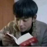 图中展示一位黑发男子，身着浅色外套，正低头专注地阅读一本红色封面的书籍。男子神情投入，视线集中在书页上，背景简洁未显示明显细节，整体氛围安静平和。