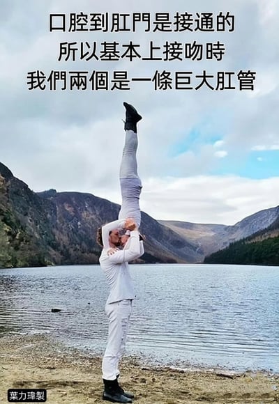 图片展示了一个在湖边山地背景下的杂技场景：一名男子站立着将另一名男子倒立举起，两人面部靠近似乎准备接吻。图片上方配有幽默文字："口腔到肛门是接通的 所以基本上接吻时 我们两个是一条巨大肛管"。这是一个基于人体解剖学的荒诞幽默梗图，通过将浪漫的接吻场景与身体消化系统的连接进行夸张联想，制造出滑稽效果。