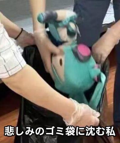 图片中显示几只手（其中一只戴着手套）正将一个绿色的毛绒玩偶（带有粉色部件和类似护目镜的装饰）放入黑色垃圾桶中。玩偶被部分挤压，显得无助。图片底部有一行日文文字“悲しみのゴミ袋に沈む私”，意为“我沉入悲伤的垃圾袋中”，通过将玩偶扔进垃圾桶的场景，隐喻人陷入悲伤情绪、感觉被丢弃的状态，整体氛围充满无奈与伤感。