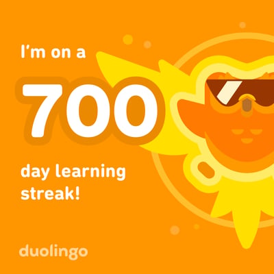 这是语言学习平台多邻国（Duolingo）的连续学习700天里程碑纪念图，整体以明亮暖橙色为背景，右侧是戴着墨镜的多邻国经典拟人化太阳卡通角色，画面中央用醒目的白色数字“700”搭配英文文字“I'm on a 700 day learning streak!”，清晰展示用户达成了700天不间断学习的记录，整体风格活泼明快，充满坚持学习的成就感。