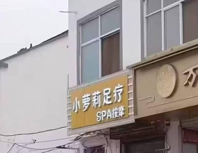 这是一张拍摄街边店铺的照片，画面主体是一家名为“小萝莉足疗”的店铺招牌，招牌为黄底白字，下方标注“SPA按摩”，店铺位于一栋白色外墙的建筑底层，旁边还能看到其他店铺的部分招牌。
该店铺名称使用“小萝莉”一词，“小萝莉”通常指代年幼的女孩，用在足疗店名称上有打擦边球、刻意吸引眼球的嫌疑，容易引发不良联想。