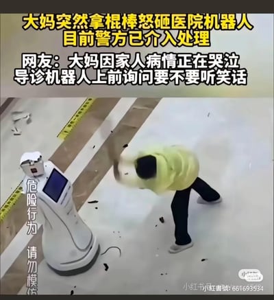 这是一段医院监控的视频截图，画面中一位身穿黄色上衣的大妈正手持棍棒用力砸向医院的白色导诊机器人，机器人周围散落着被砸落的碎片。配文信息显示，该事件是因为大妈因家人病情正在哭泣时，导诊机器人上前询问要不要听笑话，引发大妈愤怒，目前警方已介入处理。图中左侧标注有“危险行为 请勿模仿”的提示文字，整体场景充满荒诞感，是一起引发网友讨论的社会事件。